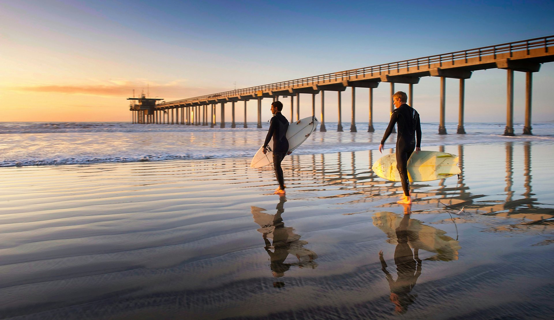 Surfers walking past Scripps Pier at sunset in La Jolla, San Diego
